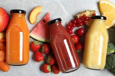 Bottles of delicious juices and fresh fruits on marble table, flat lay