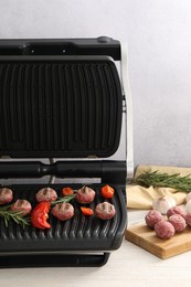 Photo of Electric grill with vegetables, meat balls and rosemary on wooden table