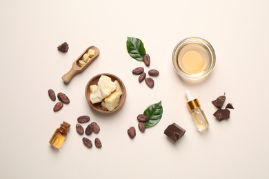 Photo of Organic cocoa butter, beans and essential oil on beige background, flat lay