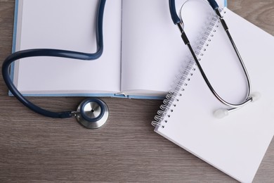 Book, stethoscope and notebook on wooden table, flat lay. Medical education