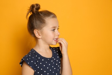 Cute little girl biting her nails on orange background, space for text