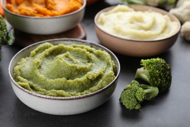 Photo of Bowls with tasty different puree and ingredients on black table, closeup