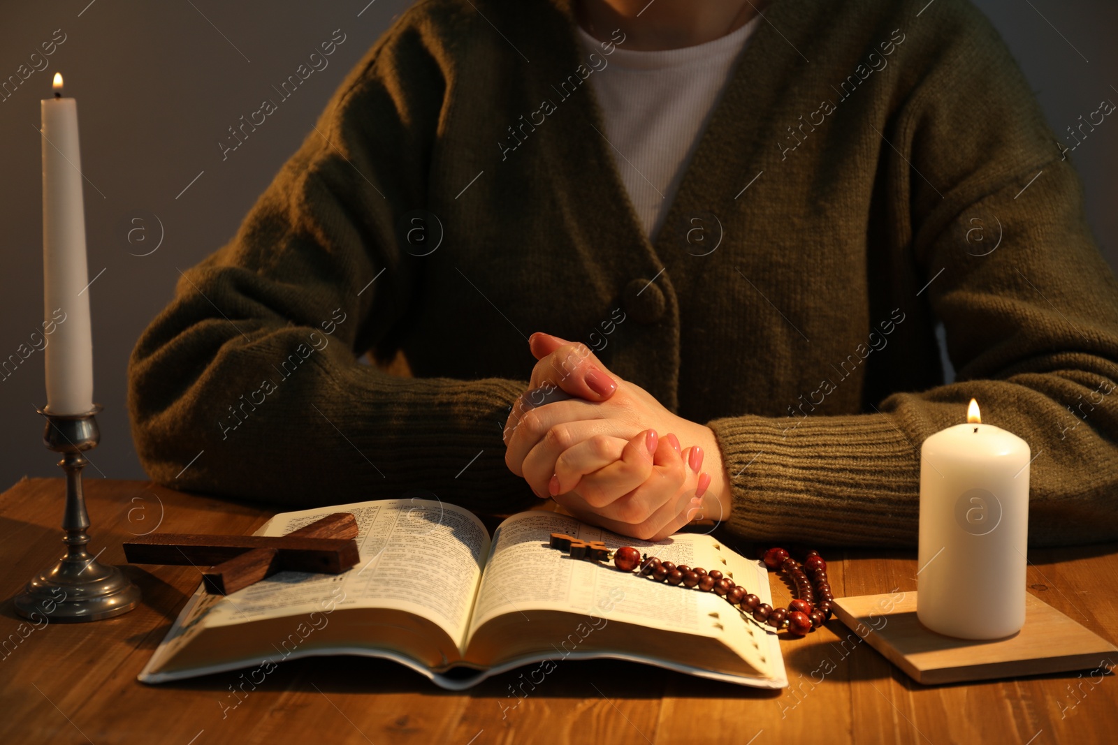 Photo of Woman praying at table with burning candles and Bible, closeup