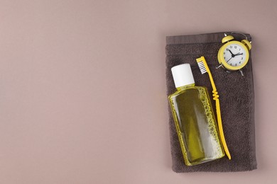Photo of Fresh mouthwash in bottle, toothbrush, alarm clock and towel on beige background, top view. Space for text