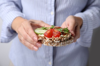 Photo of Woman holding crunchy buckwheat cakes with cream cheese, pieces of tomato and cucumber slice, closeup