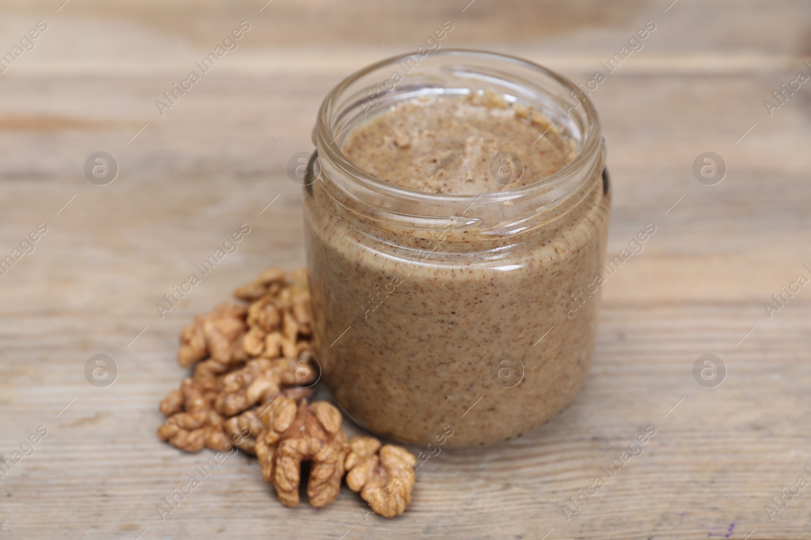 Photo of Tasty nut paste in jar and walnuts on wooden table, closeup