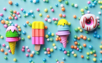 Photo of Toy ice creams, donut and beads on turquoise background, flat lay