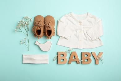 Photo of Flat lay composition with child's clothes, booties and word Baby on light blue background