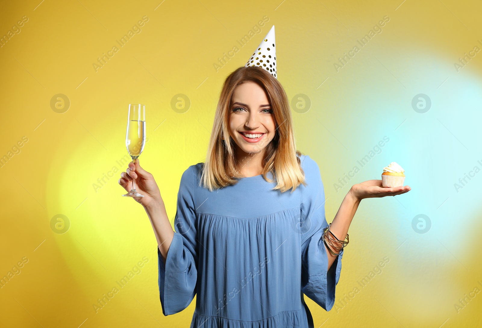 Photo of Portrait of happy woman with champagne in glass and tasty cupcake on color background