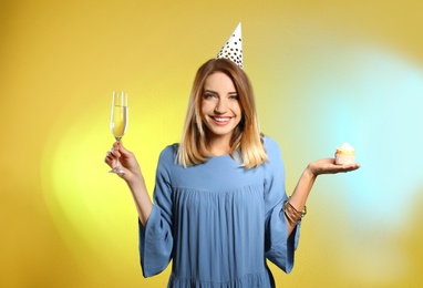 Photo of Portrait of happy woman with champagne in glass and tasty cupcake on color background