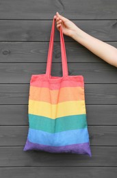 Woman holding rainbow bag against grey wooden background, closeup. LGBT pride