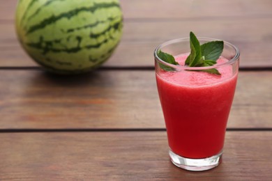 Photo of Glass of delicious watermelon smoothie with mint and fresh fruit on wooden table, closeup. Space for text