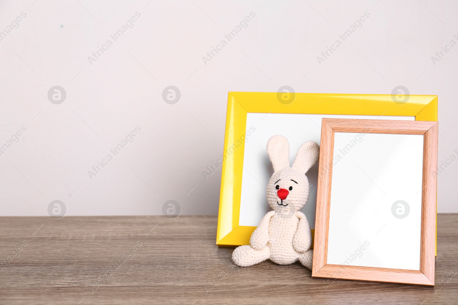 Photo of Photo frames and adorable toy bunny on table against light background, space for text. Child room elements