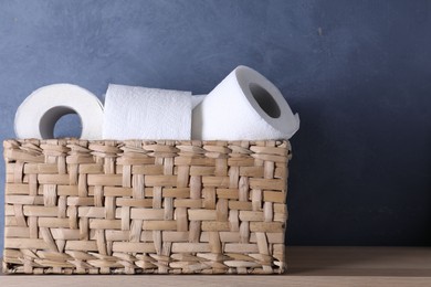 Photo of Toilet paper rolls in wicker basket on wooden table near blue wall