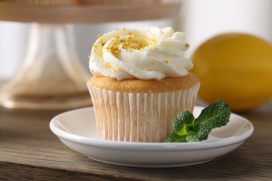 Photo of Delicious lemon cupcake with white cream and mint on wooden table, closeup