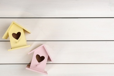 Beautiful bird houses with heart shaped holes on white wooden background, flat lay. Space for text