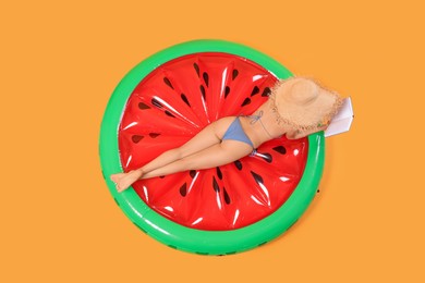 Photo of Sexy young woman with beautiful suntan and hat reading book on inflatable mattress against orange background, top view