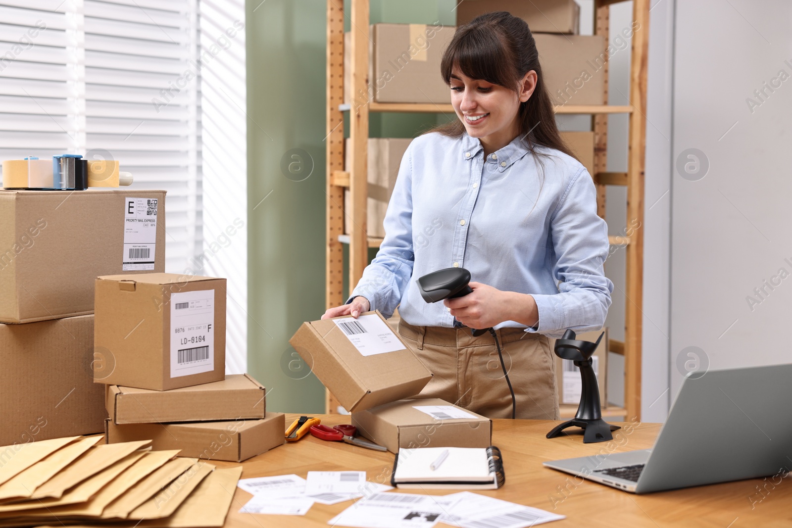 Photo of Parcel packing. Post office worker with scanner reading barcode at wooden table indoors