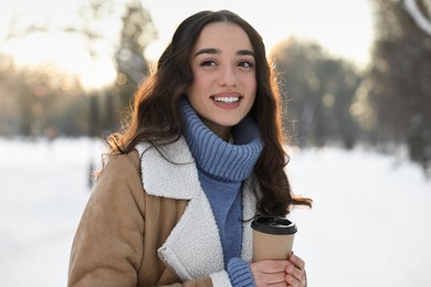 Portrait of smiling woman with paper cup of coffee in snowy park