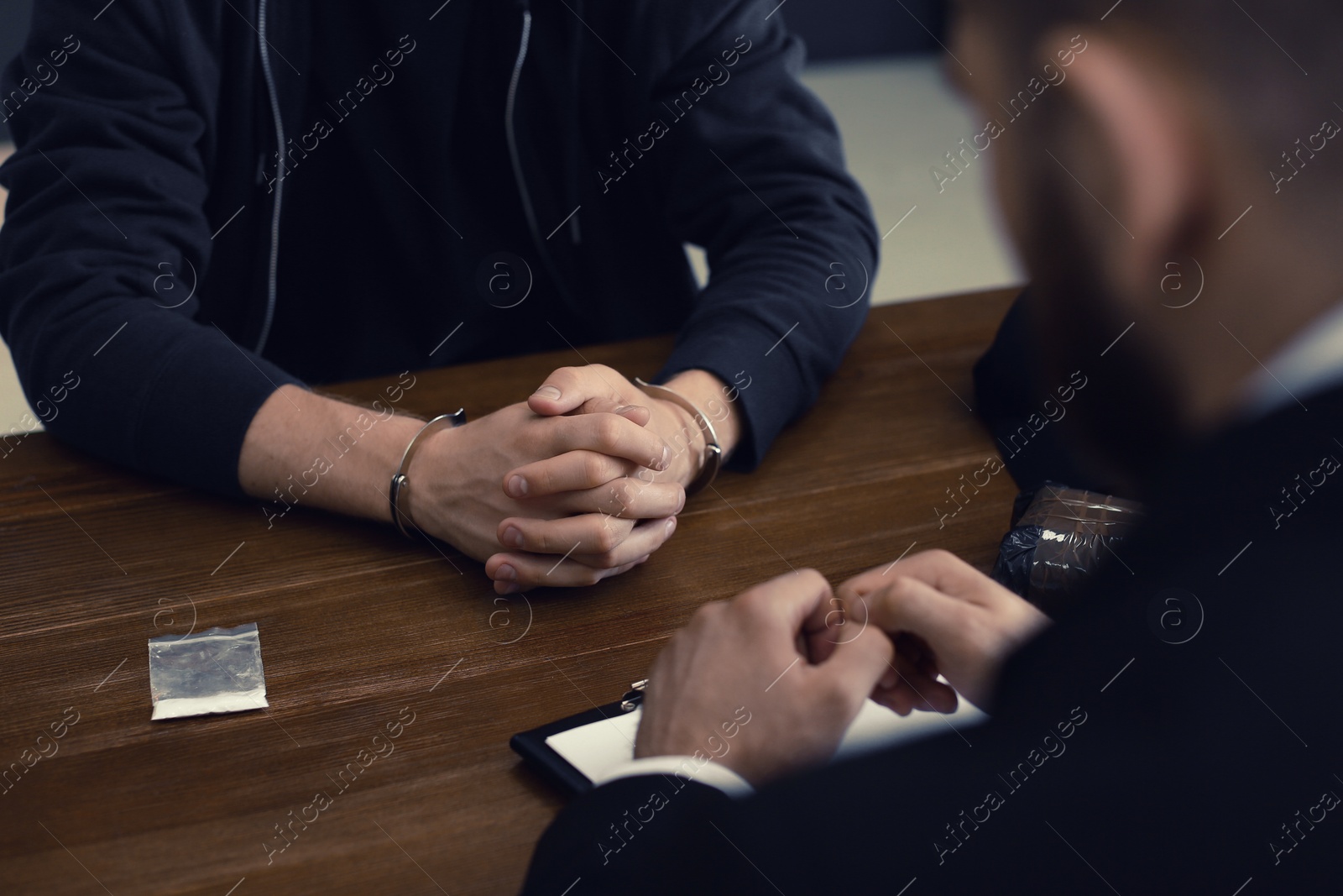 Photo of Police officer interrogating criminal in handcuffs at desk indoors