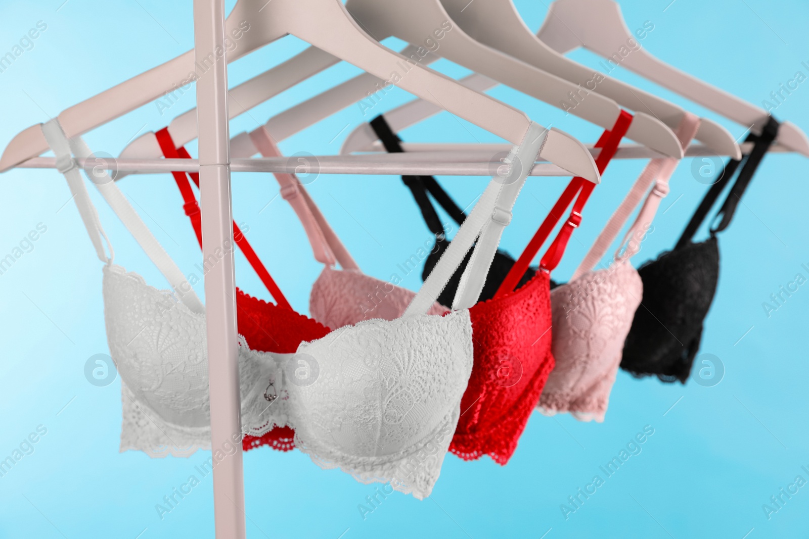Photo of Hangers with beautiful lace bras on rack against blue background. Stylish underwear