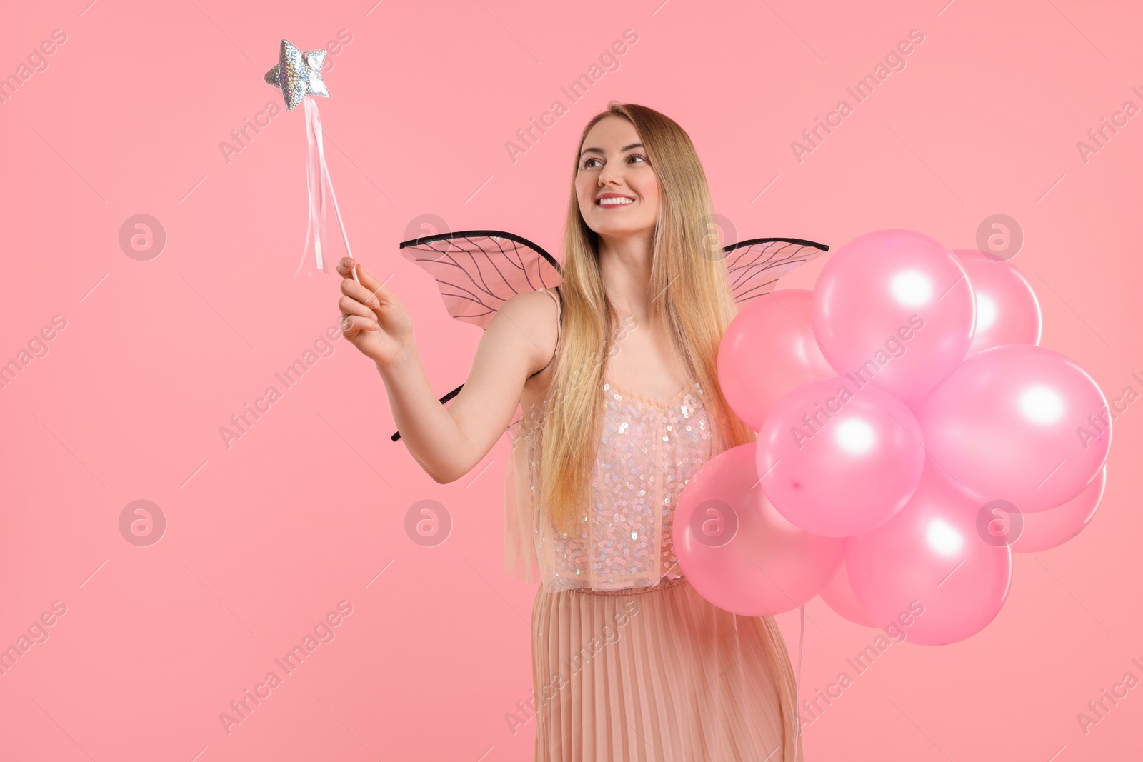 Photo of Beautiful girl in fairy costume with wings, magic wand and balloons on pink background