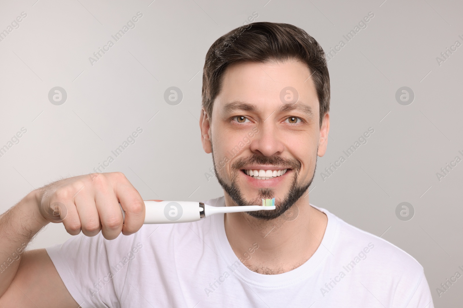 Photo of Happy man holding electric toothbrush on light grey background