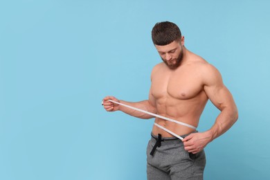 Photo of Athletic man measuring waist with tape on light blue background, space for text. Weight loss concept