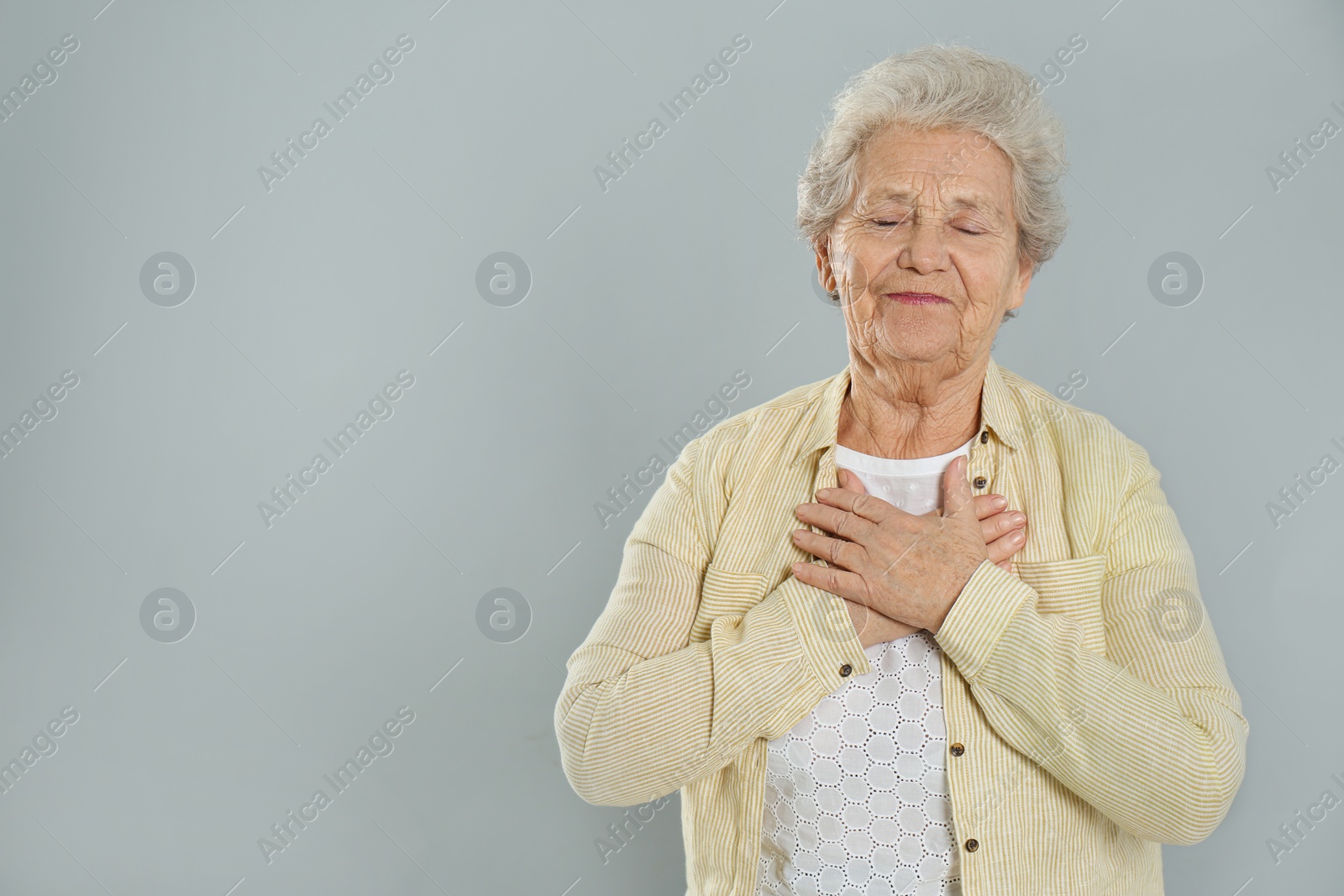 Photo of Grateful senior woman with hands on chest against grey background. Space for text