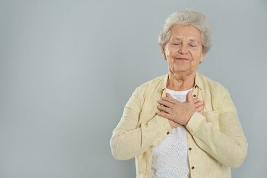 Grateful senior woman with hands on chest against grey background. Space for text