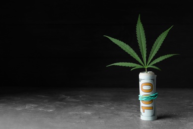 Photo of Hemp leaf and rolled money on stone grey table against black background. Space for text