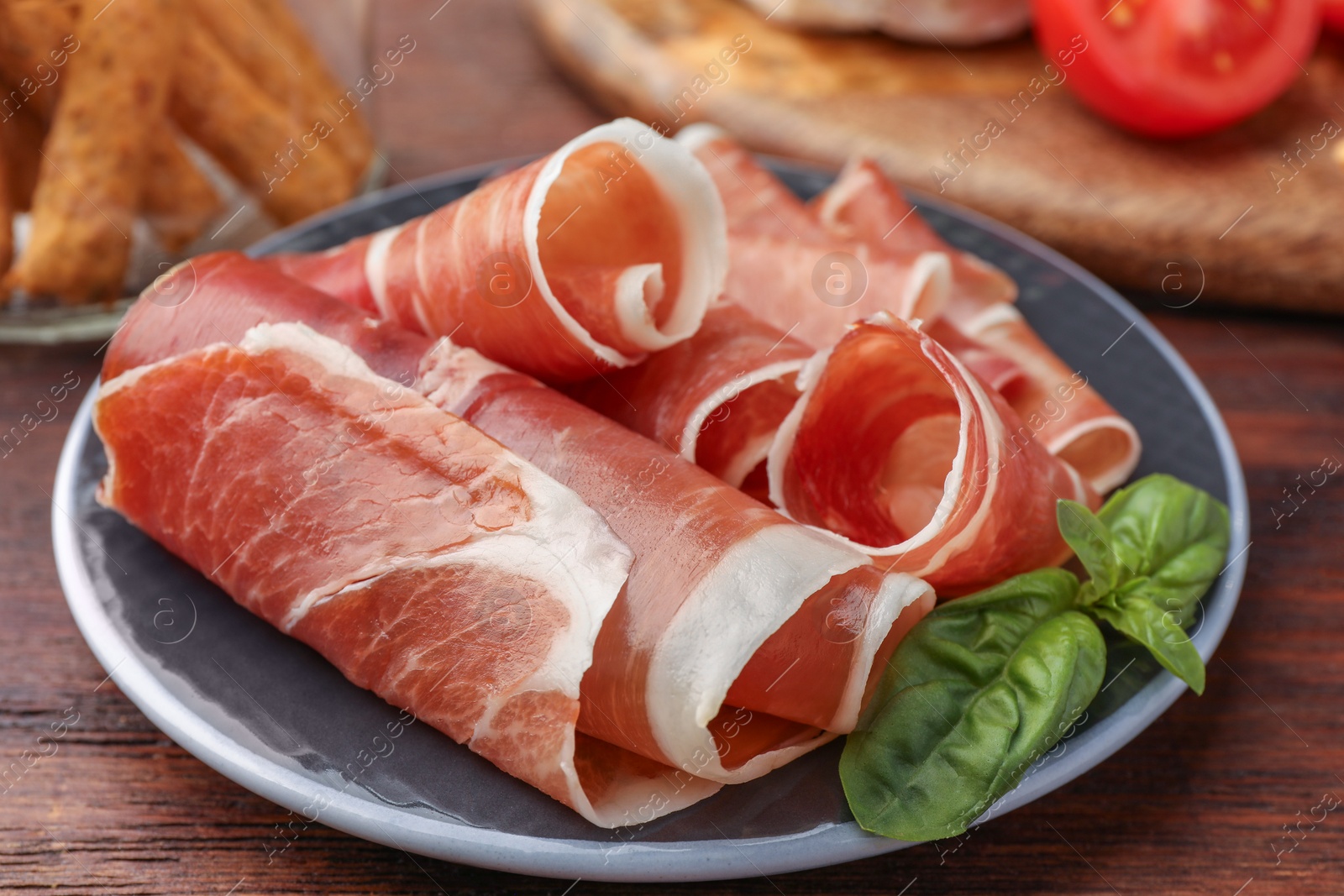 Photo of Rolled slices of delicious jamon and basil on wooden table, closeup