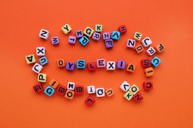 Colorful beads with word Dyslexia on orange background, flat lay