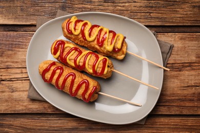 Photo of Delicious corn dogs with mustard and ketchup on wooden table, top view