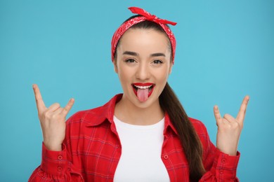 Photo of Happy woman showing her tongue and rock gesture on light blue background