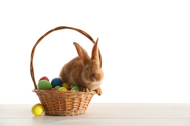 Cute bunny and basket with Easter eggs on table against white background. Space for text