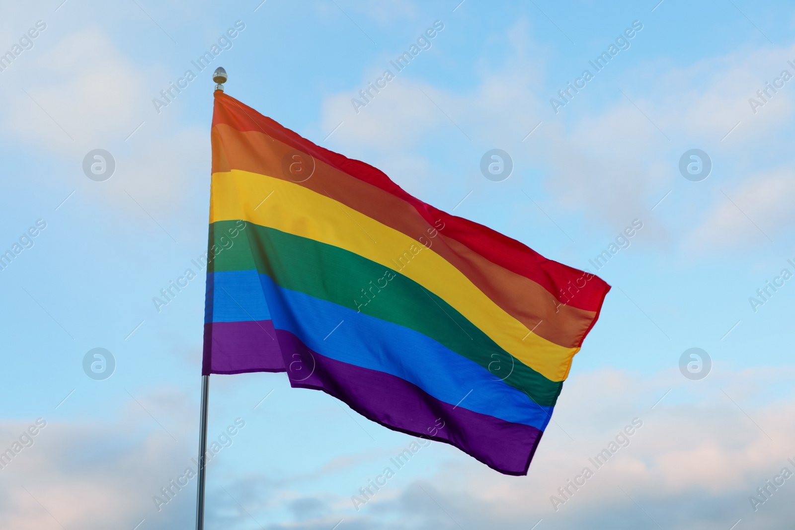 Photo of Bright LGBT flag against blue sky with clouds