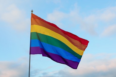 Bright LGBT flag against blue sky with clouds