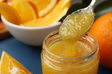 Photo of Spoon and jar with delicious orange marmalade on table, closeup. Space for text