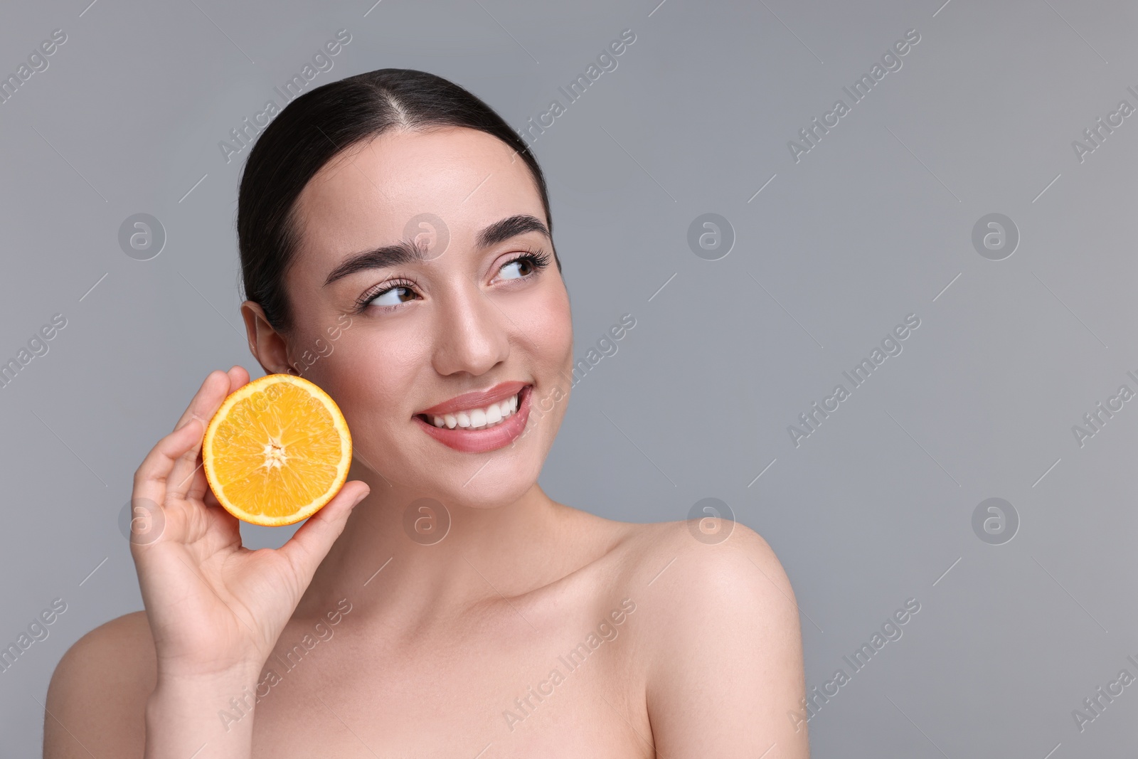 Photo of Beautiful young woman with piece of orange on grey background. Space for text