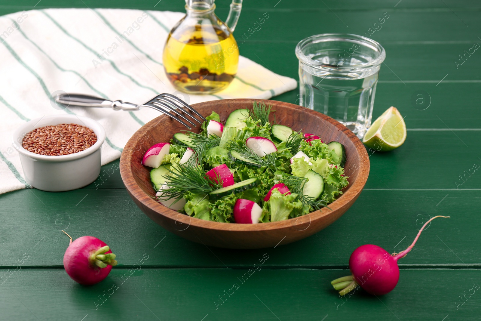 Photo of Delicious salad with radish, lettuce, dill and cucumber served on green wooden table