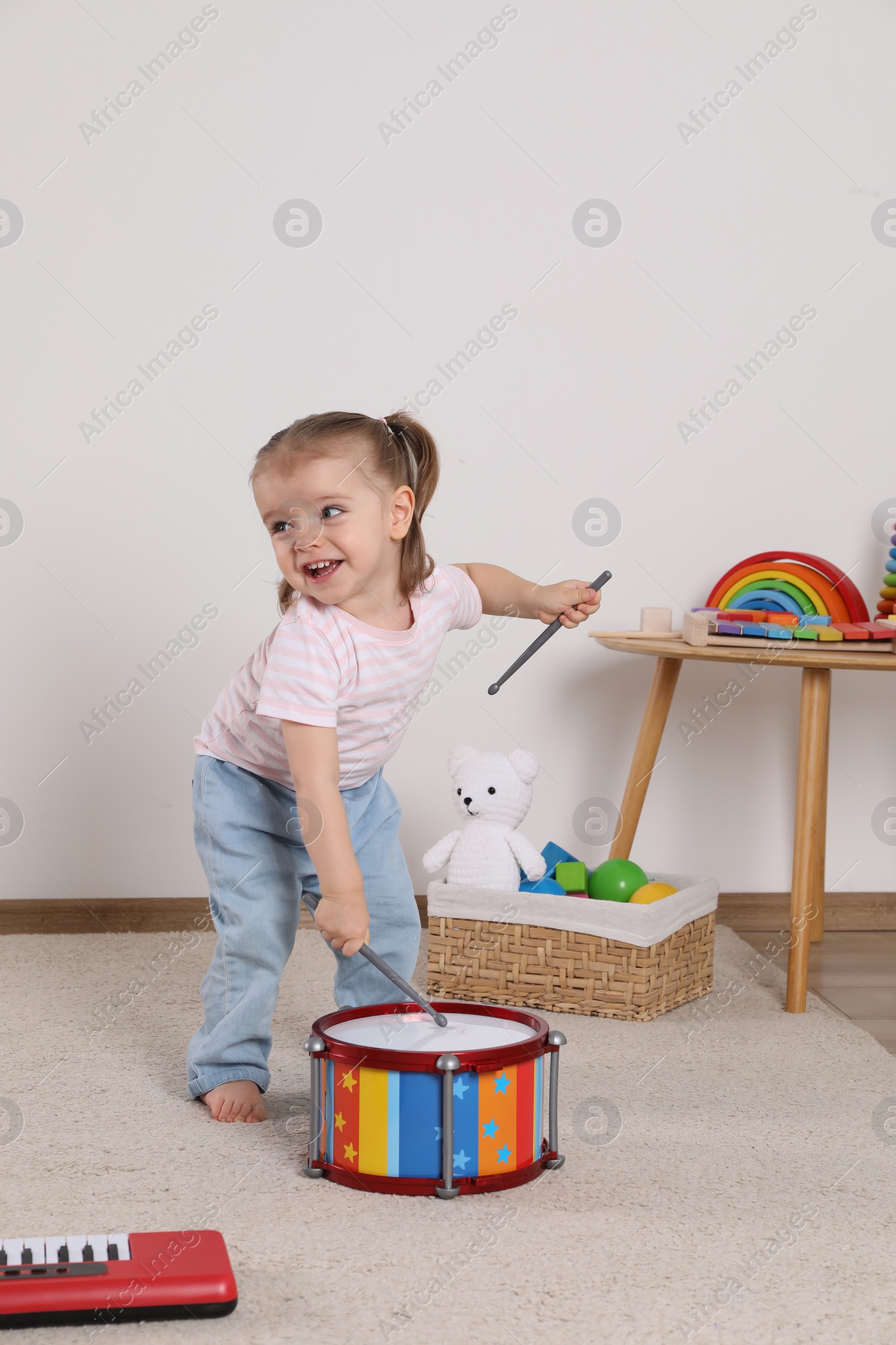 Photo of Cute little girl playing with drum and drumsticks at home