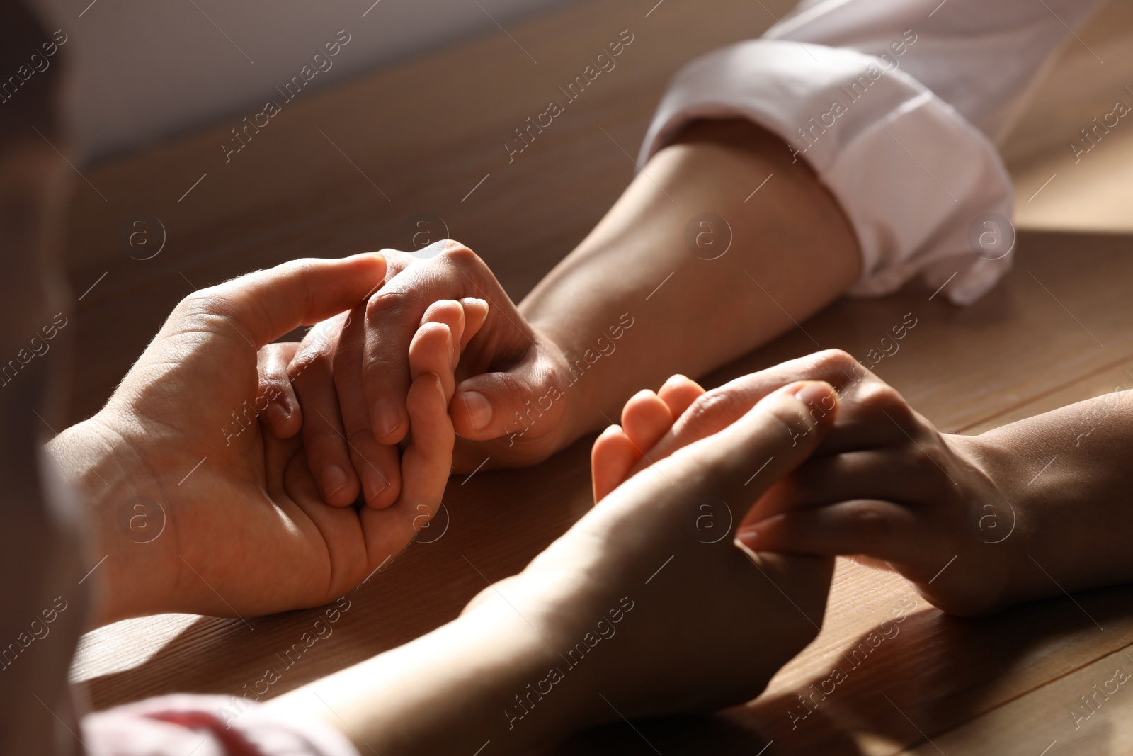 Photo of Religious women holding hands and praying together at wooden table, closeup