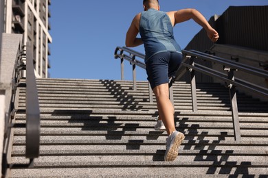 Photo of Man running up stairs outdoors on sunny day, back view