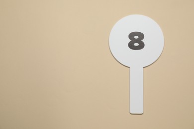 Photo of Auction paddle with number 8 on beige background, top view. Space for text