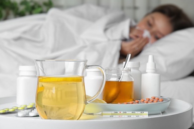 Hot lemon tea with different cold remedies on white table and sick woman on background