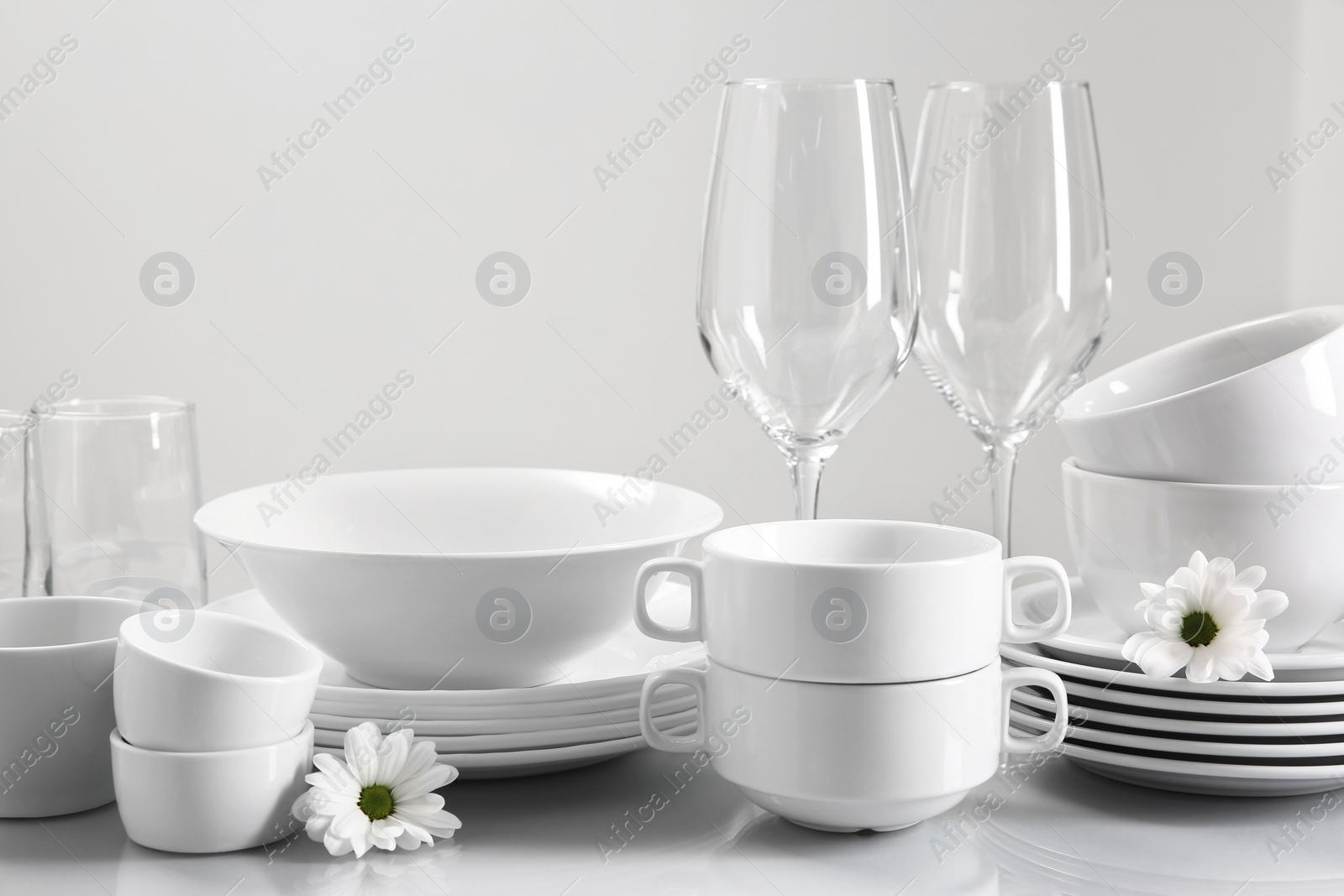 Photo of Set of many clean dishware, flowers and glasses on light table