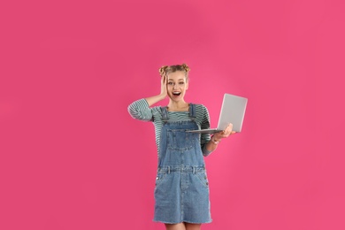 Portrait of young woman with laptop on pink background