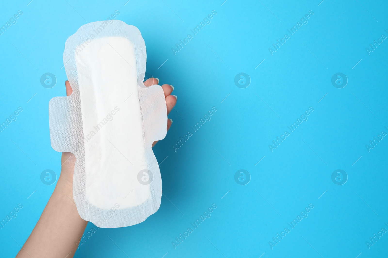 Photo of Woman holding sanitary napkin on light blue background, closeup. Space for text