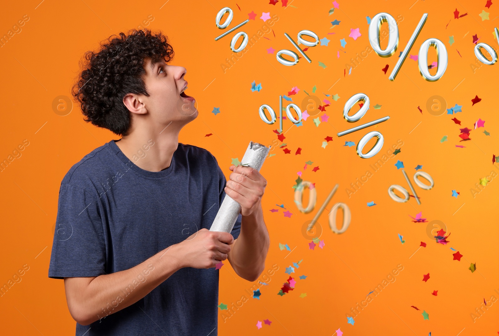 Image of Discount offer. Happy young man blowing up party popper on orange background. Confetti and percent signs in air
